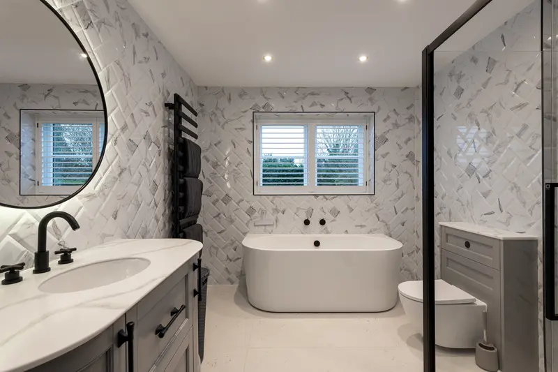 Bathroom with freestanding bath, marble-effect tiles and a round mirror