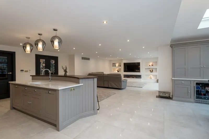 Open-plan kitchen with painted island leading to a living area with media wall